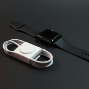 Close-up of a black smartwatch and white charging cable on a dark surface. Ideal for technology themes.